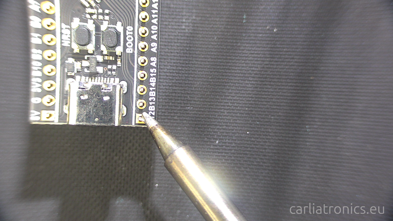 A solder iron tip on a pad demonstrating how to heat pad and pin